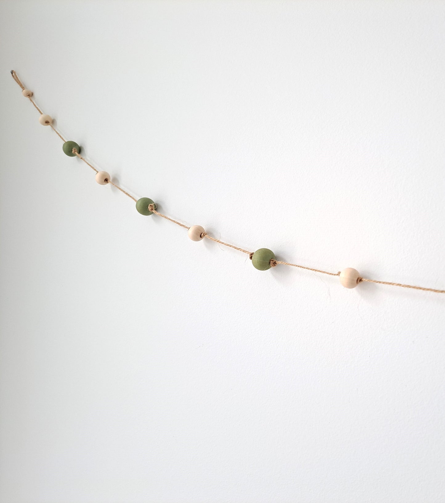 Weathered Landing's handmade sage green and natural wood bead garland. Beautiful in a nursery or on a fireplace mantel for a Scandi, boho, or modern farmhouse feel. Works great with neutral decor and is made with wood and jute. Find wooden bead garlands at Weathered Landing. Located in Komoka, Ontario. Shipping to Canada and US.
