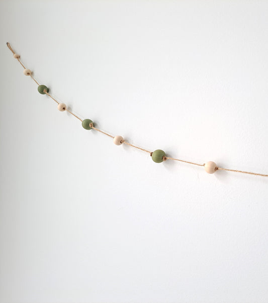 Weathered Landing's handmade sage green and natural wood bead garland. Beautiful in a nursery or on a fireplace mantel for a Scandi, boho, or modern farmhouse feel. Works great with neutral decor and is made with wood and jute. Find wooden bead garlands at Weathered Landing. Located in Komoka, Ontario. Shipping to Canada and US.