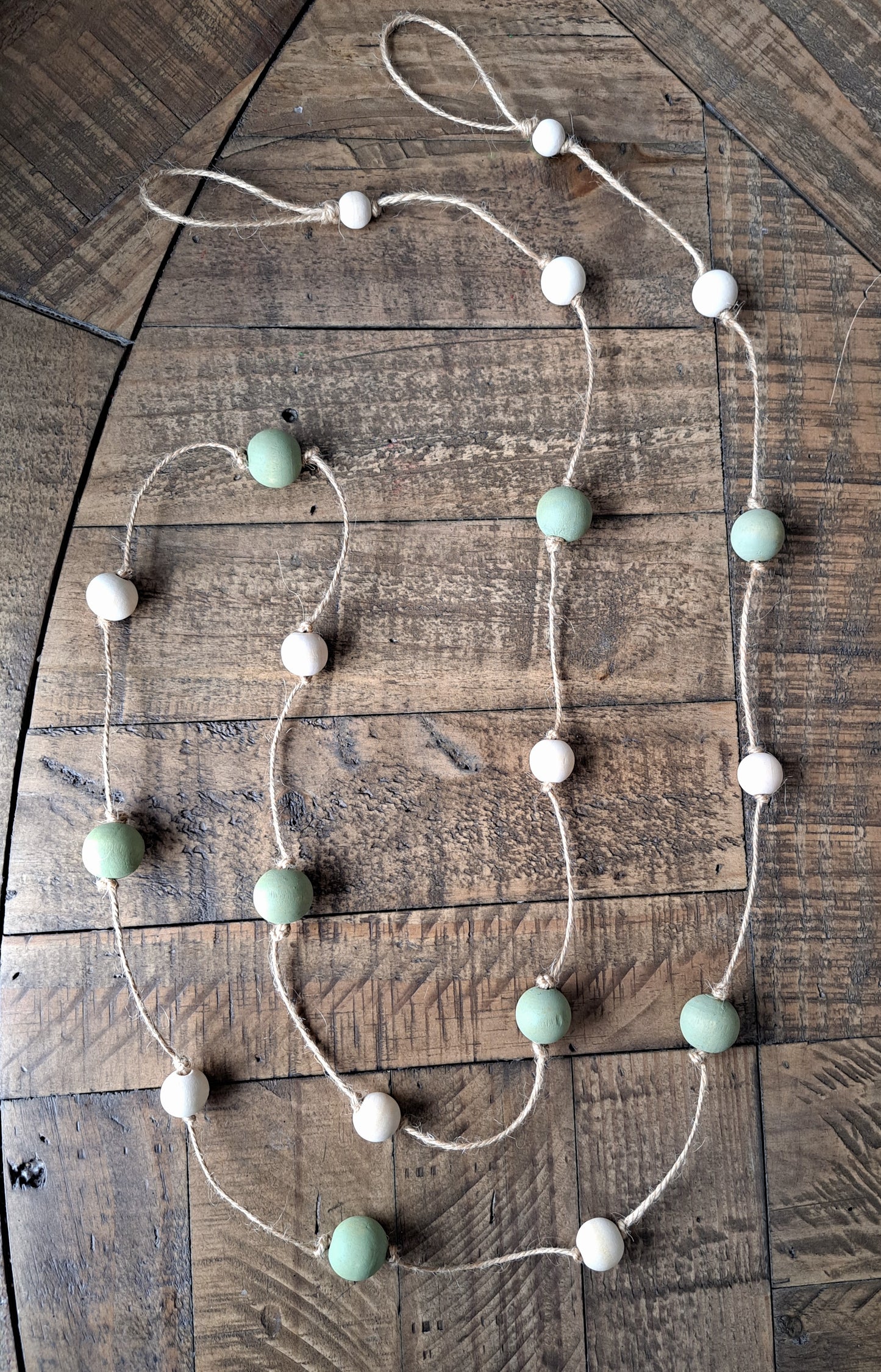 Weathered Landing's handmade sage green and natural wood bead garland. Beautiful in a nursery or on a fireplace mantel for a Scandi, boho, or modern farmhouse feel. Works great with neutral decor and is made with wood and jute. Find wooden bead garlands at Weathered Landing. Located in Komoka, Ontario. Shipping to Canada and US.