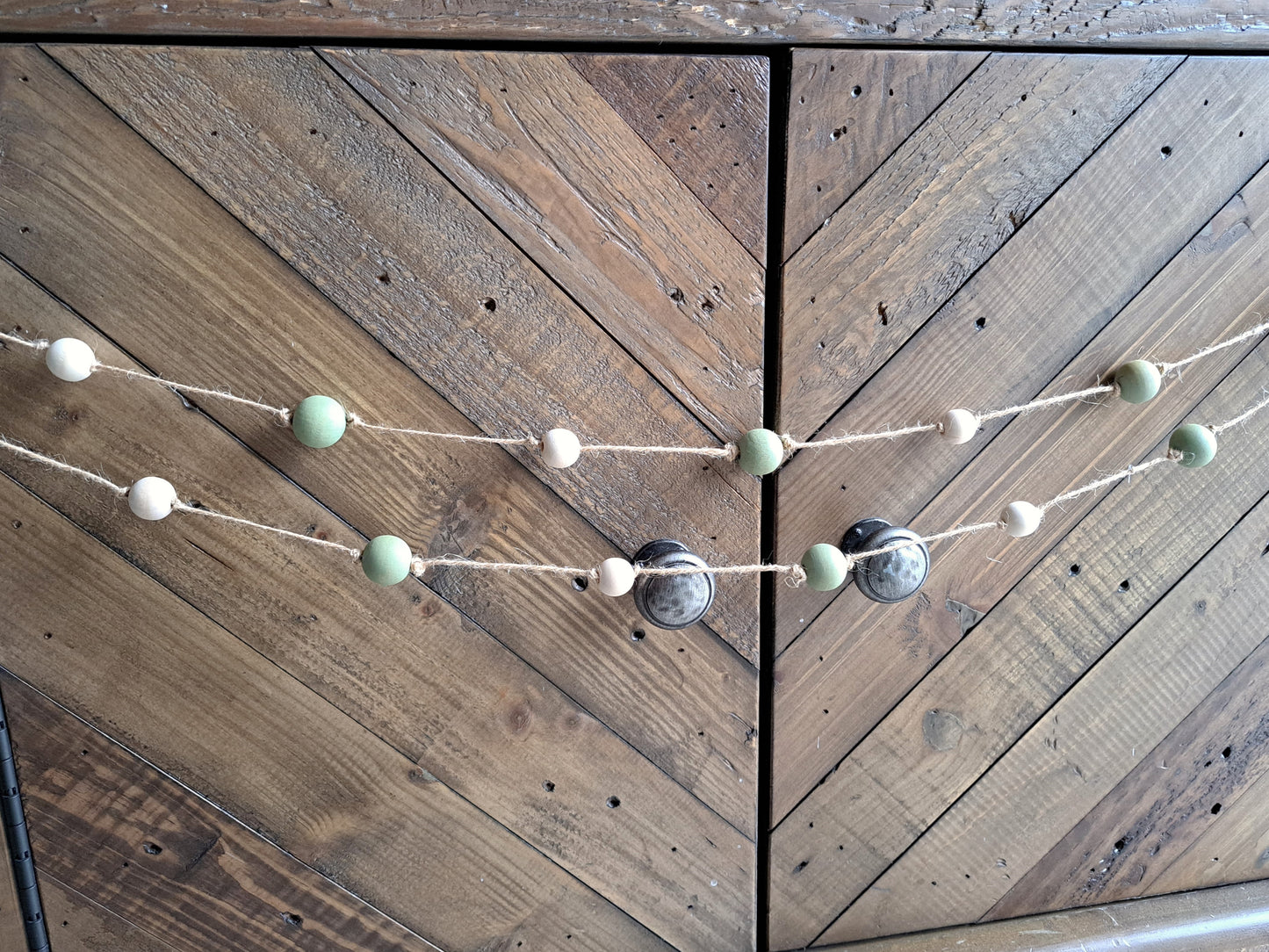 Weathered Landing's handmade sage green and natural wood bead garland. Beautiful in a nursery or on a fireplace mantel for a Scandi, boho, or modern farmhouse feel. Works great with neutral decor and is made with wood and jute. Find wooden bead garlands at Weathered Landing. Located in Komoka, Ontario. Shipping to Canada and US.