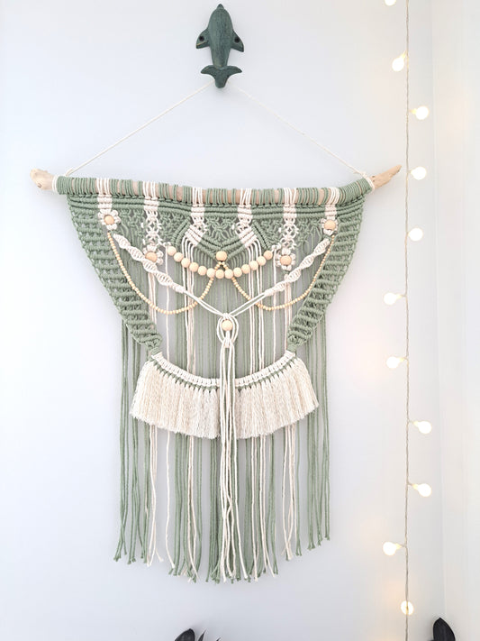 Weathered Landing's Boho Macrame Driftwood Wall Hanging. Handmade with sage green and white cotton macrame, wooden beads, and driftwood, this carefully crafted boho wall hanging is delicate and dainty. Perfect for a nursery or a bedroom nook. With lots of contrast in colour, texture, and pattern, this eclectic macrame wall hanging adds a bohemian feel to the space. Shipping to Canada and US.
